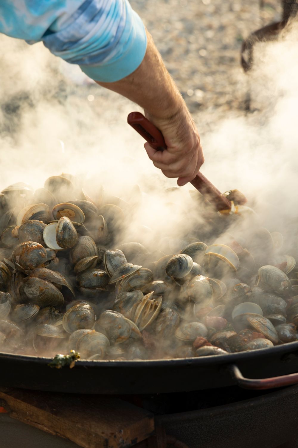 A hand tosses clams in a large pan