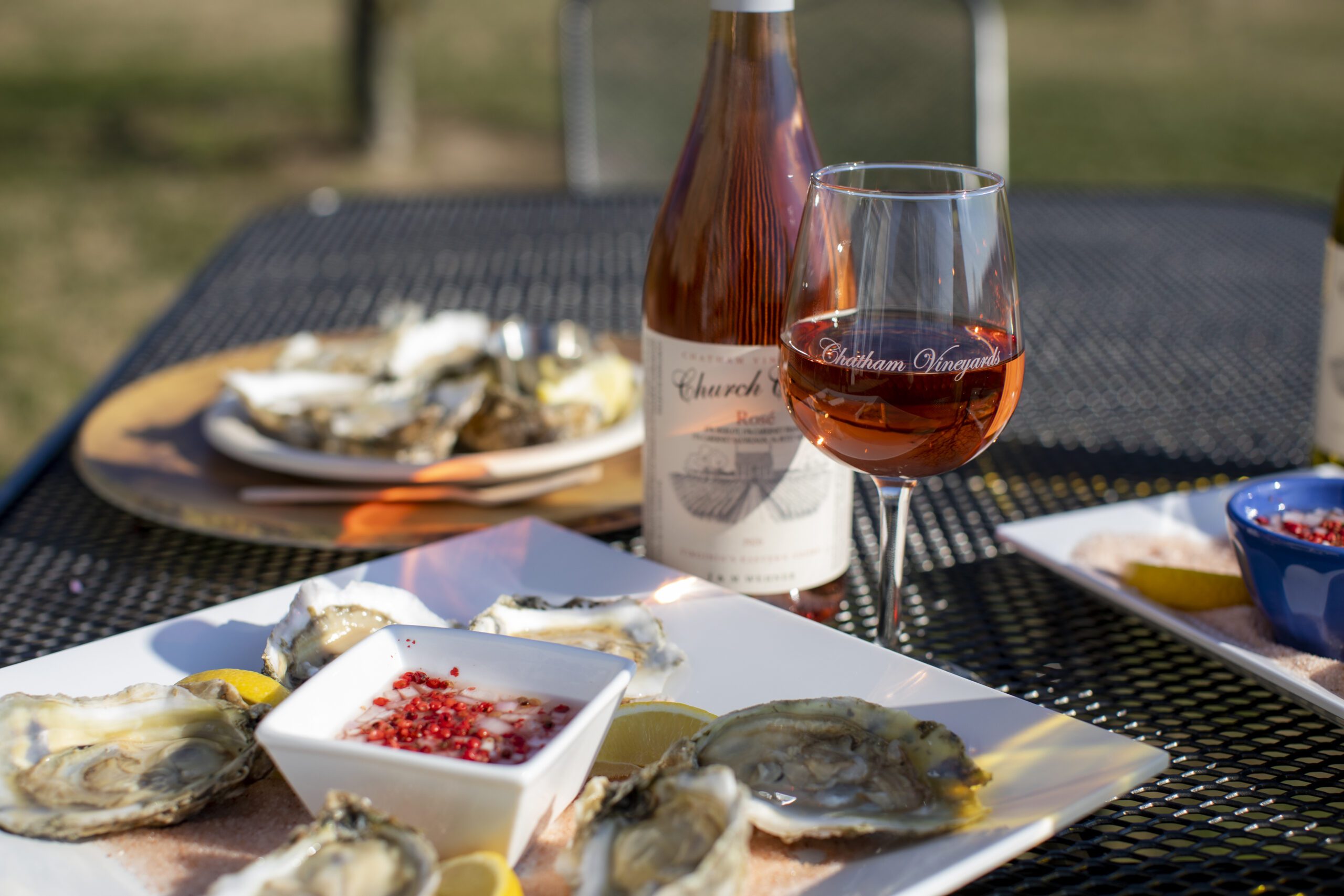 A bottle and glass of wine from Chatham Vineyards on a table with plates of oysters