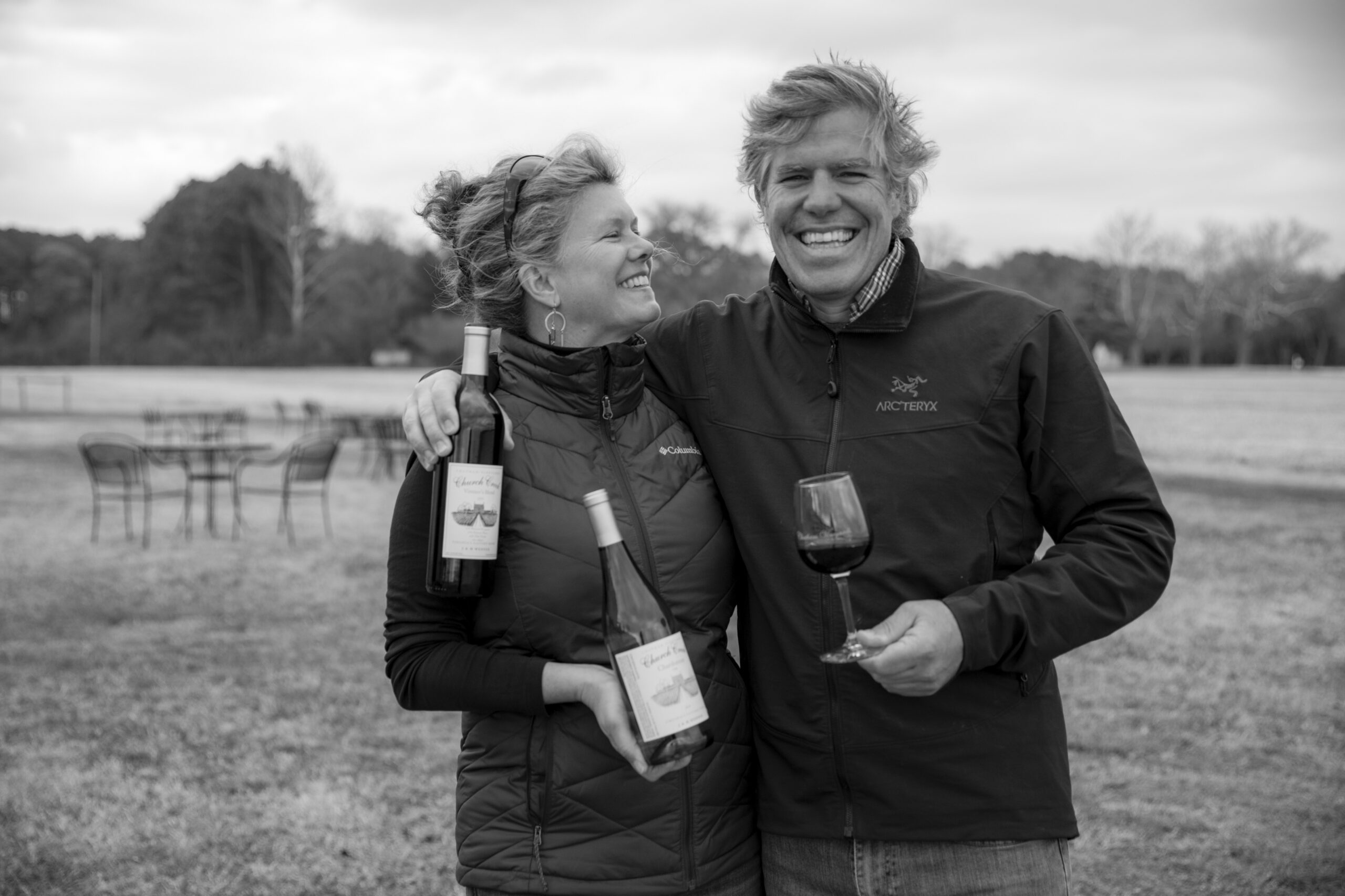 A man and a woman pose while holding a bottle and a glass of Chatham Vineyards wine