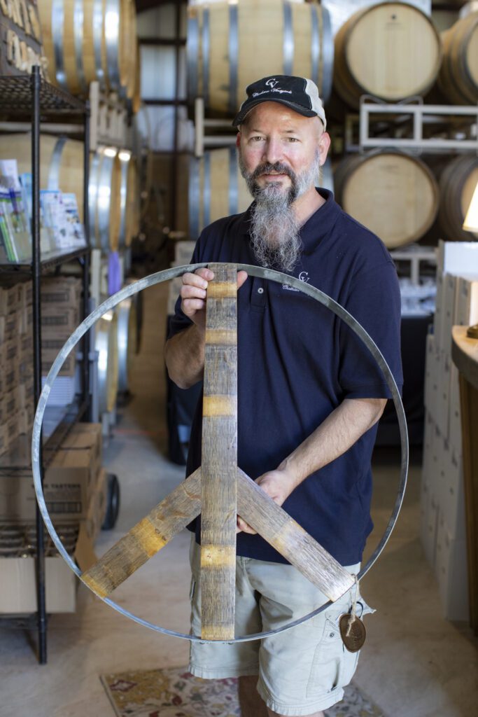 Ethan Watkins holding a peace sign he created with repurposed wine barrels