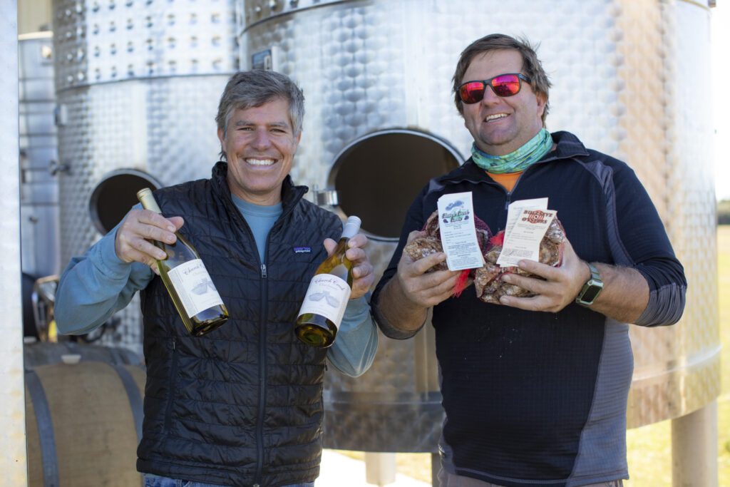 Jon Wehner from Chatham Vineyards and Tom Gallivan  from Shooting Point Oysters each hold Chatham Vineyards wine and smile for the camera