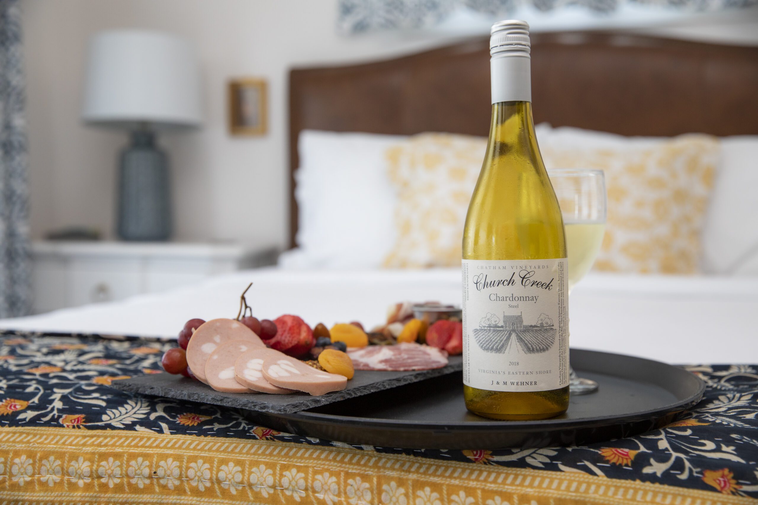 bottle of Chatham Vineyards wine and a charcuterie board placed on a bed in an inn on the Eastern Shore of Virginia